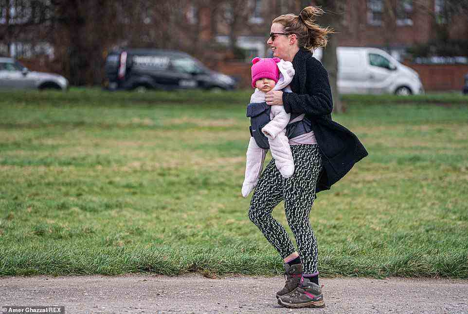 A woman carries her baby during strong winds this morning on Wimbledon Common in South West London