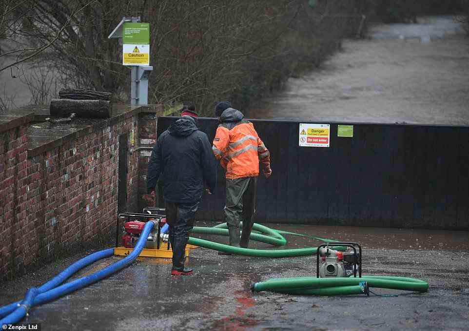 Workmen stand at the floodgates in Didsbury, Greater Manchester, as they check water is flowing into surrounding fields