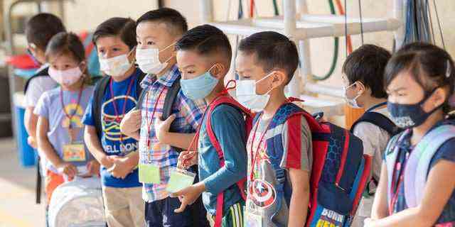 Maskierte Schüler warten darauf, am ersten Unterrichtstag der Stanford Elementary School in Garden Grove, Kalifornien, am 16. August 2021 in ihr Klassenzimmer zu gehen. Schüler und Lehrer mussten im Klassenzimmer Masken tragen, aber nicht draußen. 