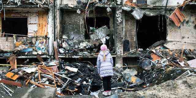 Am 25. Februar 2022 blickt ein Mädchen in Kiew, Ukraine, auf den Krater, den eine Explosion vor einem Wohnhaus hinterlassen hat, das während laufender Militäroperationen schwer beschädigt wurde.