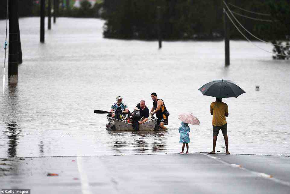 A family use a tinny to cross waters in Logan after the river flooded the area south of Brisbane on Sunday morning