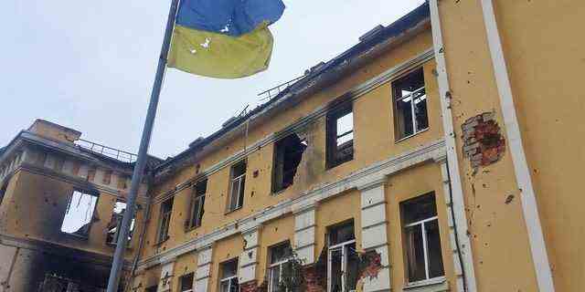 Die ukrainische Nationalflagge ist am 28. Februar 2022 in Charkiw, Ukraine, vor einer Schule zu sehen, die nach Angaben von Anwohnern nach dem Beschuss in Flammen stand, während Russlands Invasion in der Ukraine andauert. 