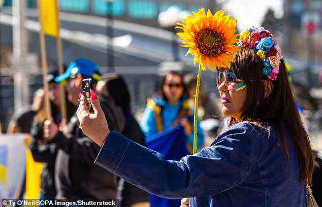 A woman is picture taking a selfie while holding a flower at a U.S. protest against Russia's invasion of Ukraine