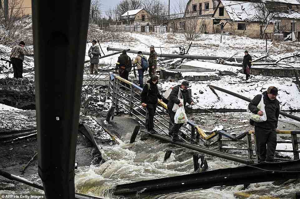 Civilians try to cross a river on a blown up bridge carrying food and other supplies, to the north of Kyiv