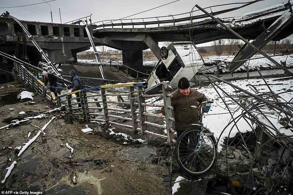 A man pushing a bicycle crosses a destroyed bridge on the outskirts of Kyiv today