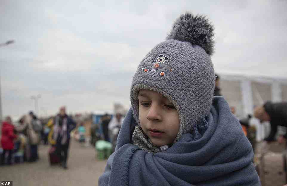 A child wrapped in a blanket and woolly hat attempts to keep warm as his family waits to cross the border into Poland