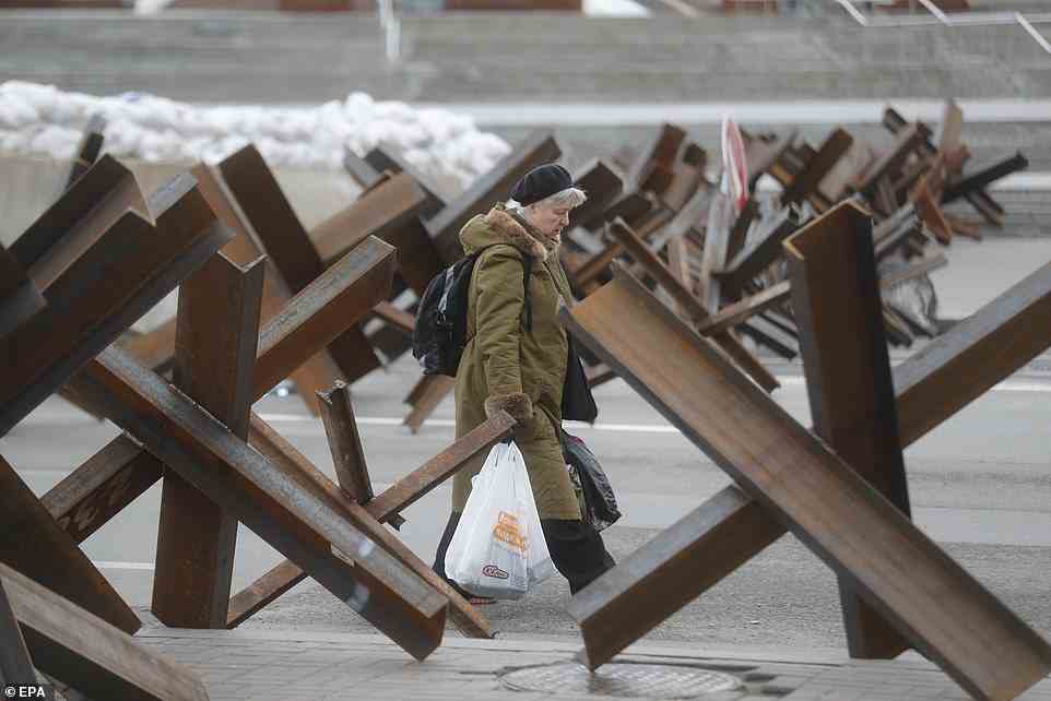 A woman is pictured today carrying bags while walking past Czech hedgehogs in downtown Kyiv