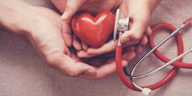 Kind und Erwachsener, die rotes Herz mit Stethoskop halten.