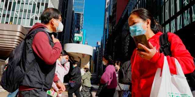 Menschen mit Gesichtsmasken gehen am Mittwoch, dem 9. März 2022, über eine Hauptstraße in einer Straße in der Innenstadt von Hongkong. 