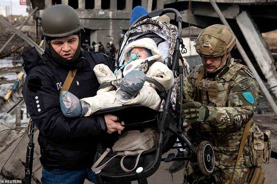 A baby is evacuated as people flee near a destroyed bridge to cross the Irpin River, on the outskirts of Kyiv, as Russian forces try to surround it in ahead of an attack