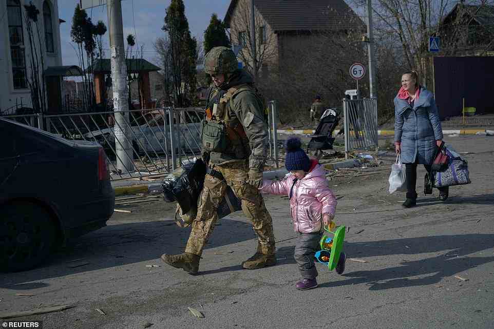 A member of the military holds a young child's hands as civilians flee the country after two weeks of sustained attacks from Russia
