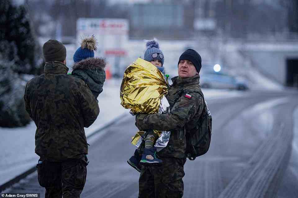 Polish soldiers hold Ukrainian refugees after they crossed the border during snowfall to Medyka, Poland