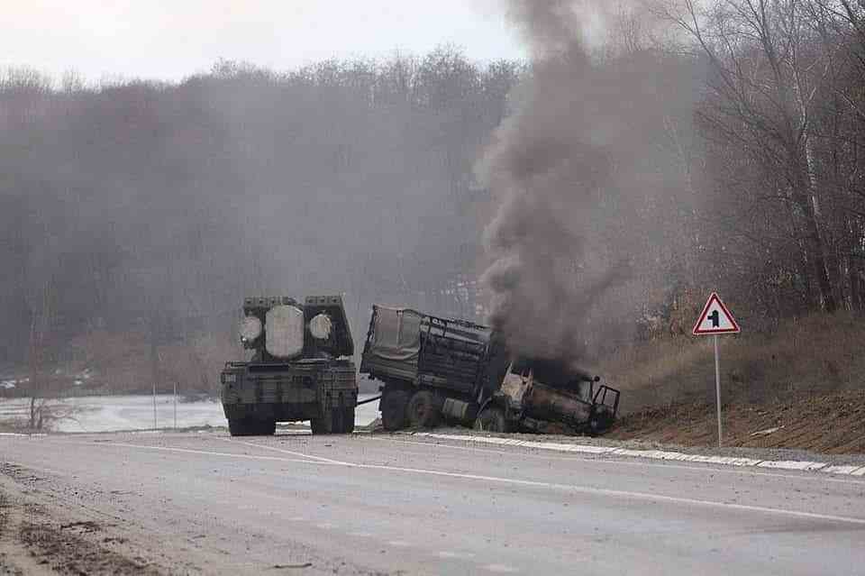 A destroyed Russian supply truck burns next to an abandoned vehicle, along a highway somewhere in Ukraine