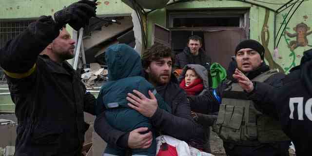 Ein Mann trägt sein Kind aus dem durch Beschuss zerstörten Entbindungsheim in Mariupol, Ukraine