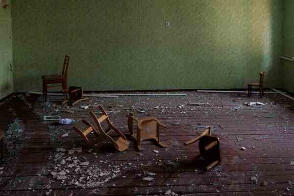 A green room with broken glass and damaged child-sized chairs.