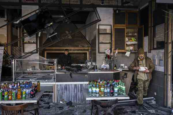 A damaged restaurant. Part of the ceiling has fallen down. Bottled drinks are stacked on tables.