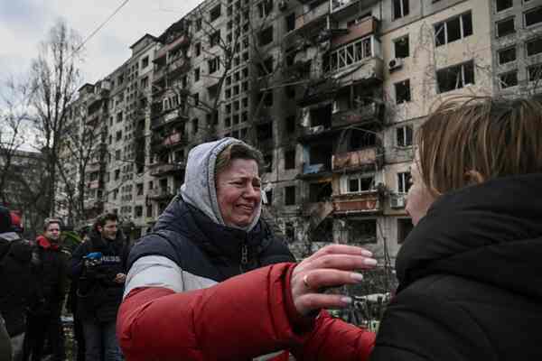 Two women hug in front of a burned building.