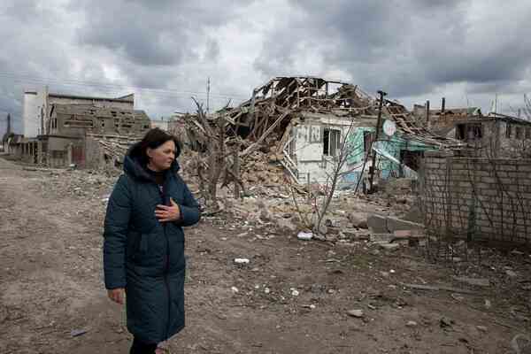 A woman walks by collapsed houses.