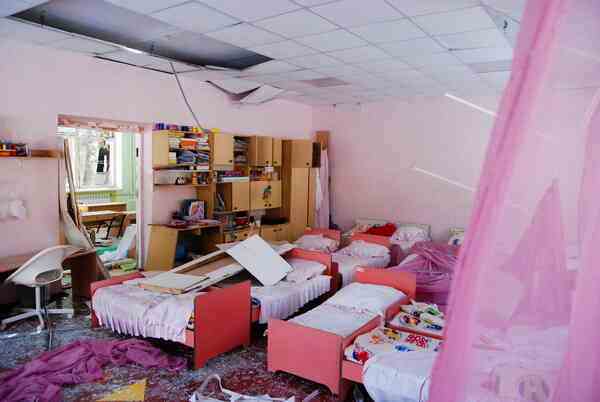 A pink room full of small beds. Some of the ceiling panels have fallen down.