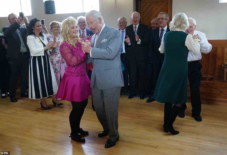 Everyone looking on as Prince Charles and Camilla have a good time dancing with volunteers while learning about the tradition Irish dance