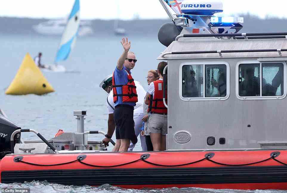 The Duke of Cambridge waves to cheering crowds on a boat as he stands alongside his wife Kate Middleton