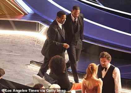 Denzel Washington can be seen smiling as he walks an emotionally charged Will Smith back to his seat in the front row in the Dolby Theatre