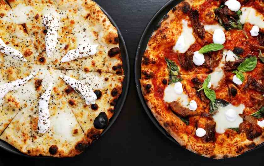 Ein Overhead-Foto von zwei Pizzana-Pizzen auf einer schwarzen Tischplatte.