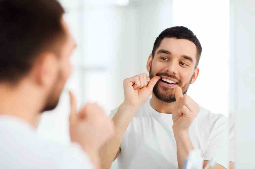 Mann benutzt Zahnseide, während er in den Spiegel schaut