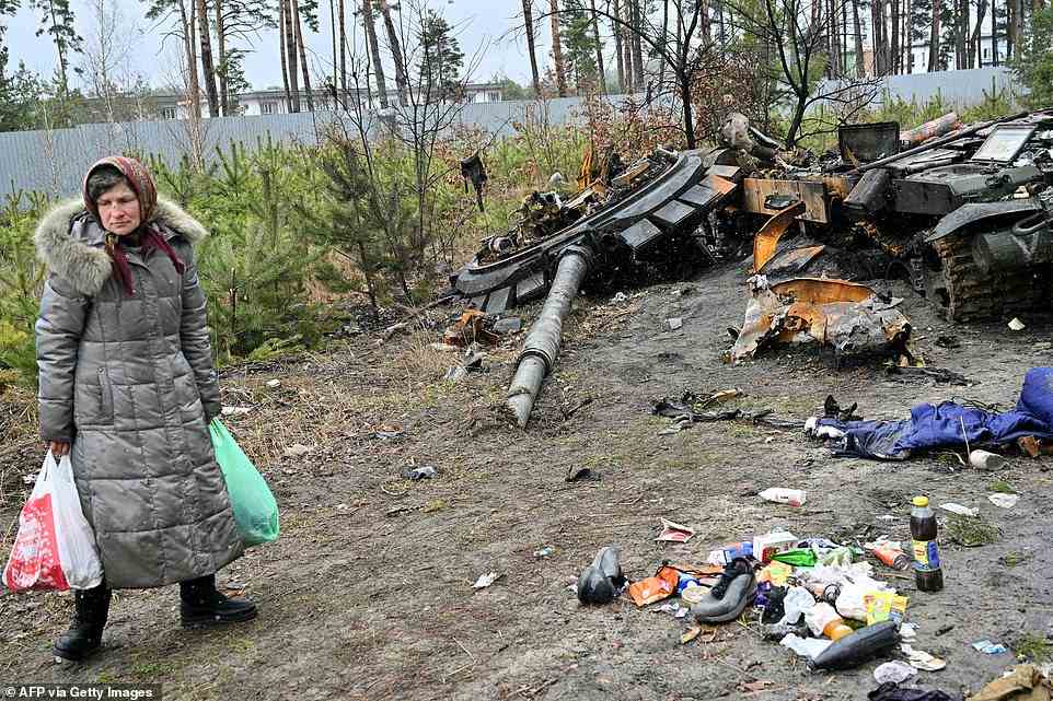 A woman carrying two shopping bags walks past a destroyed Russian army tank, not far from the Ukrainian capital of Kyiv