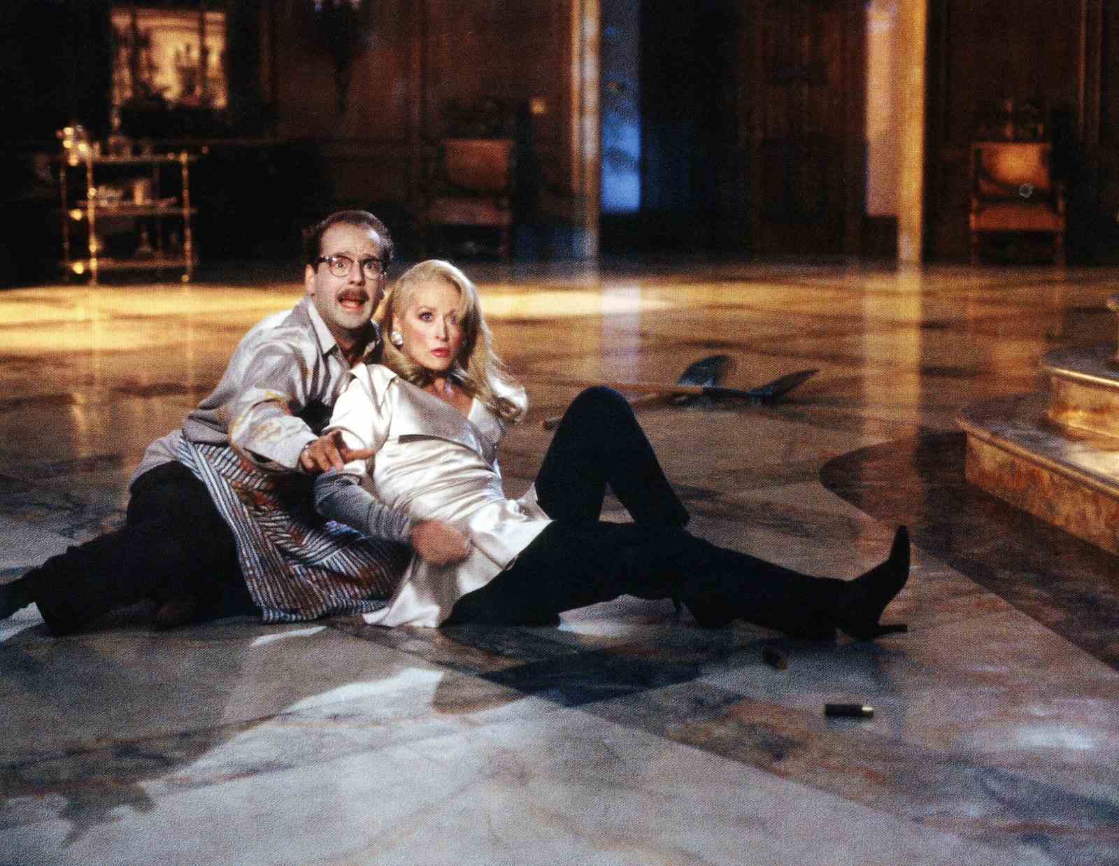 Bruce Willis und Meryl Streep sitzen in „Death Becomes Her“ auf dem Boden und starren in die Kamera.