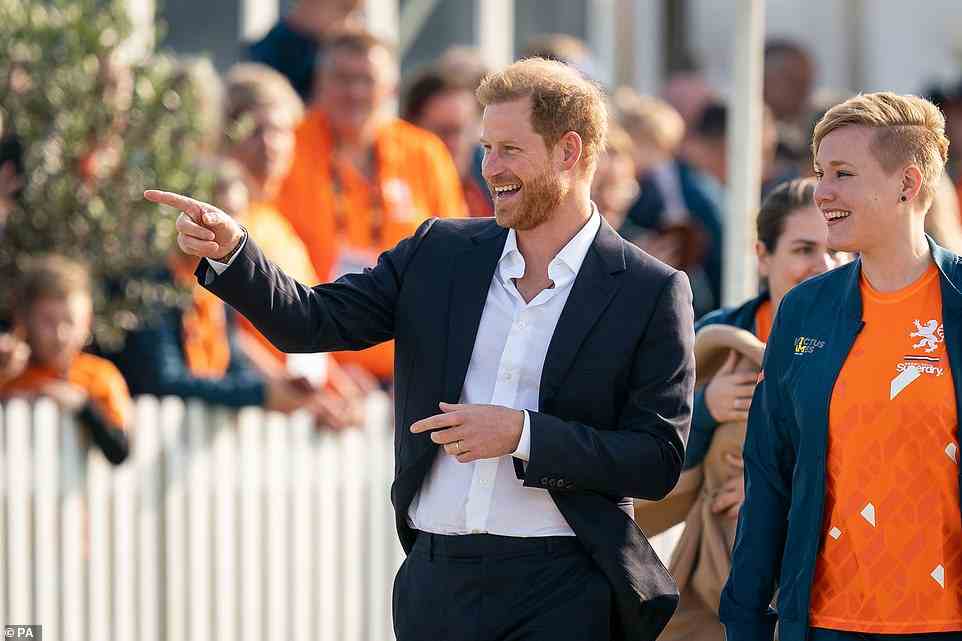 Harry smiles and points at the cheering crowd, as he and Meghan head to the reception event