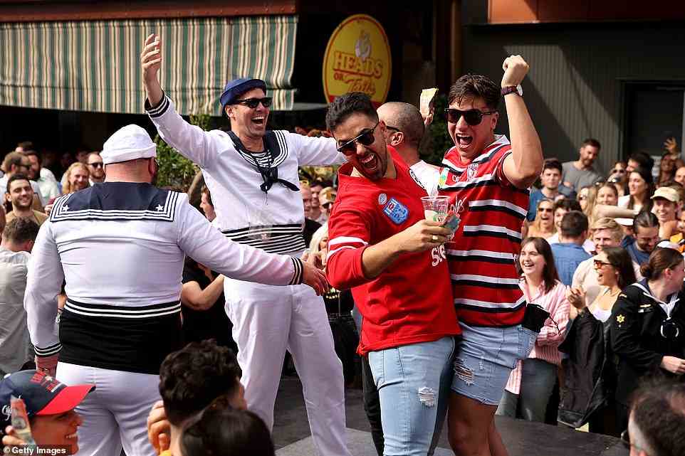 A group of men wearing sailor outfits embrace and cheer as they drink VB after placing successful bets during two-up