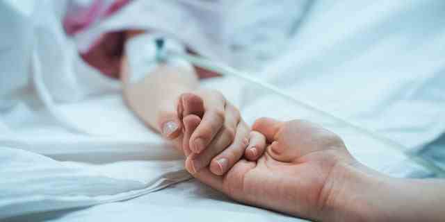 Ein Kind in einem Krankenhausbett hält die Hand seiner Eltern.