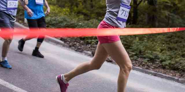 Glückliche Frau, die ein Marathonrennen gewinnt und die Ziellinie mit erhobenem Arm überquert.