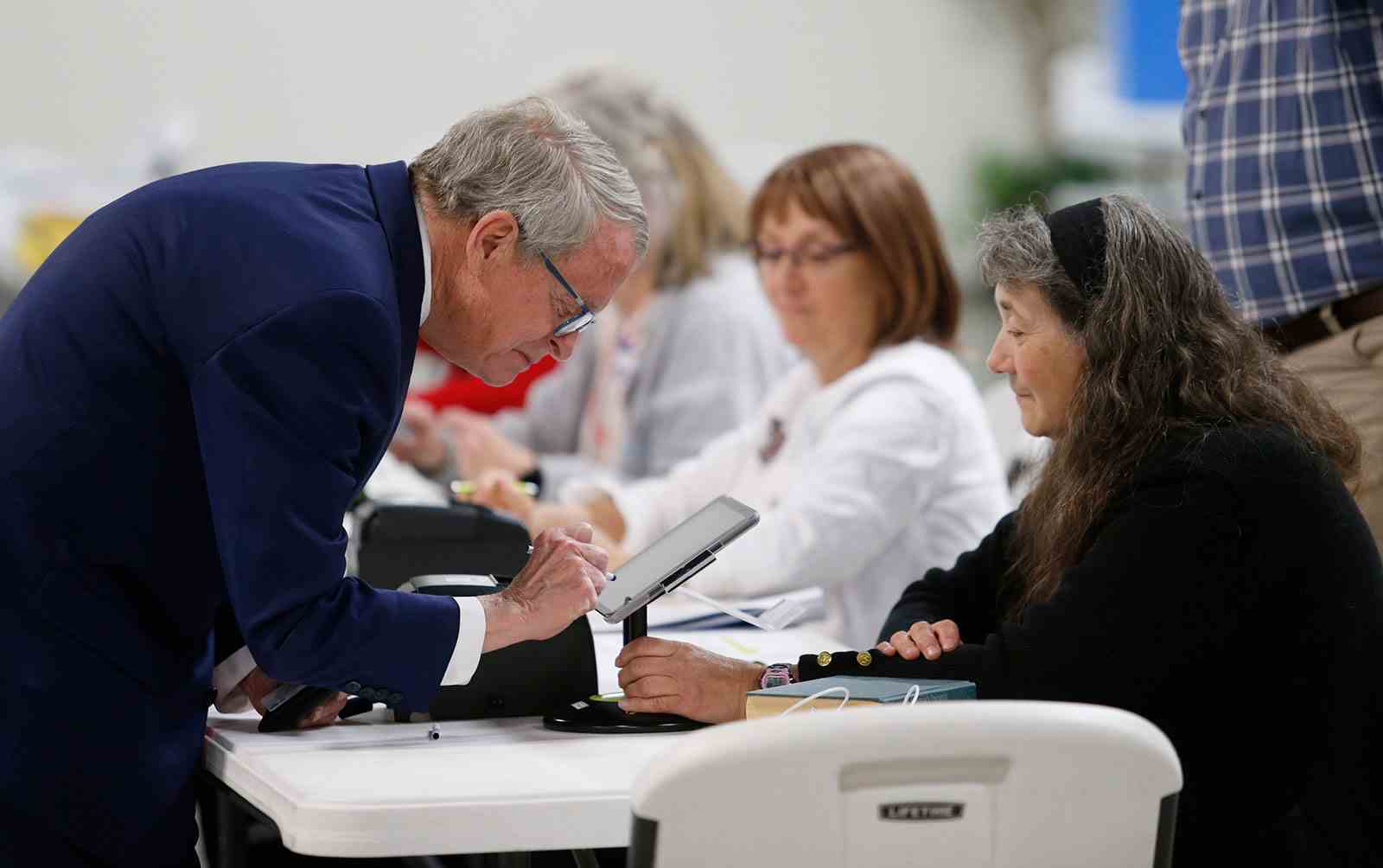 Mike DeWine, Gouverneur von Ohio, links, unterschreibt für seinen Stimmzettel vor der Bezirksmitarbeiterin Tonya Veldt, während er sich auf die Abstimmung am Dienstag, den 3. Mai in Cedarville, Ohio, vorbereitet.