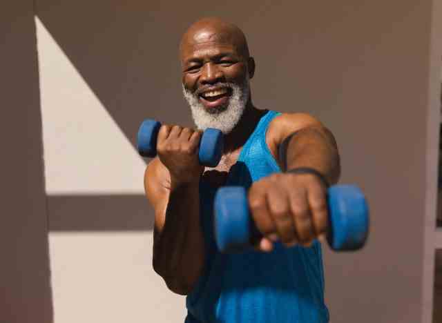 Glücklicher, fitter Mann in den 50er Jahren, der Hanteln für das HIIT-Training hält, um den Bauchfettabbau zu beschleunigen