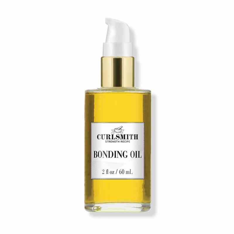 A clear glass pump bottle of the gold-hued Curlsmith Bonding Oil on a white background
