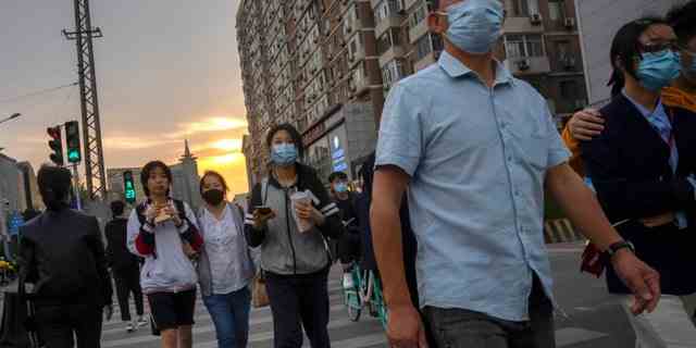 Menschen mit Gesichtsmasken gehen während der abendlichen Hauptverkehrszeit in Peking am Mittwoch, den 20. April 2022, über eine Kreuzung. (AP Photo/Mark Schiefelbein)