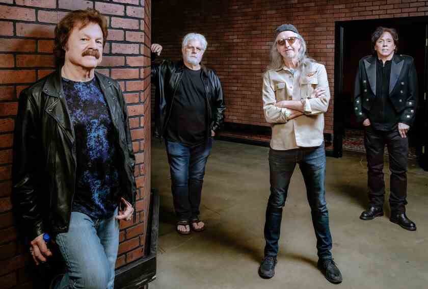 Vier Männer einer Rockband stehen in einem Flur vor Backsteinwänden