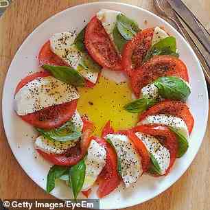 Ein Caprese-Salat besteht normalerweise aus nur drei Zutaten – Mozzarella-Käse, Basilikum und Tomaten.  Wenn Sie also die roten Früchte entfernen, erhalten Sie einfach einen Teller mit geschnittenem Käse mit etwas Basilikum (Stockfoto)