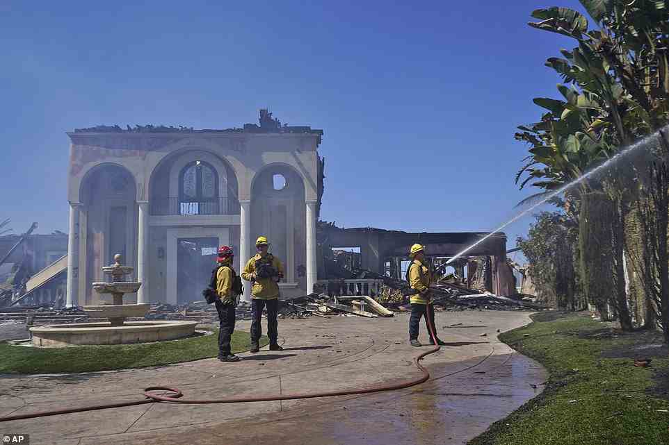 Members of the Torrance Fire Dept, from left, Brent Nunez, Michael Cotter and Rick Cathey protect the remains of a fire-damaged home in the aftermath of the Coastal Fire
