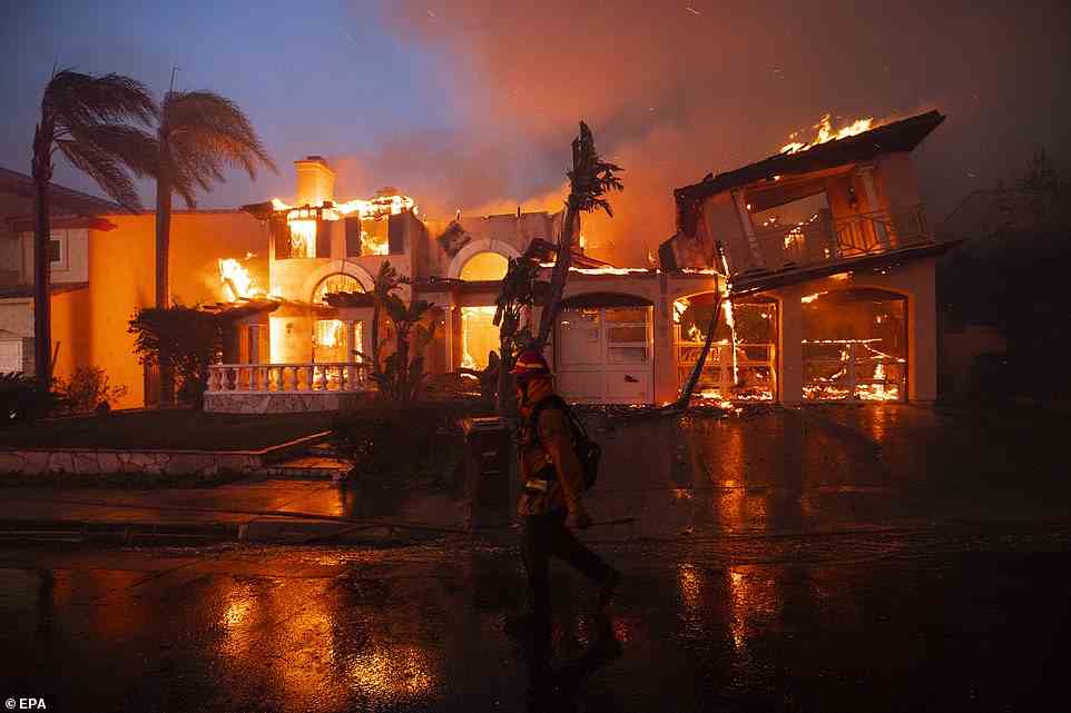 A firefighter walks past a mansion on fire caused by the Coastal Fire in Laguna Niguel on Wednesday night