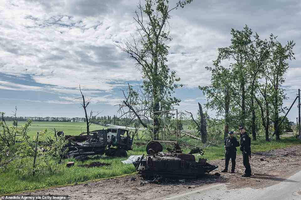 Ukrainian policemen are seen in front of the wreckage of a tank as a destroyed military vehicle is seen behind in Kharkiv