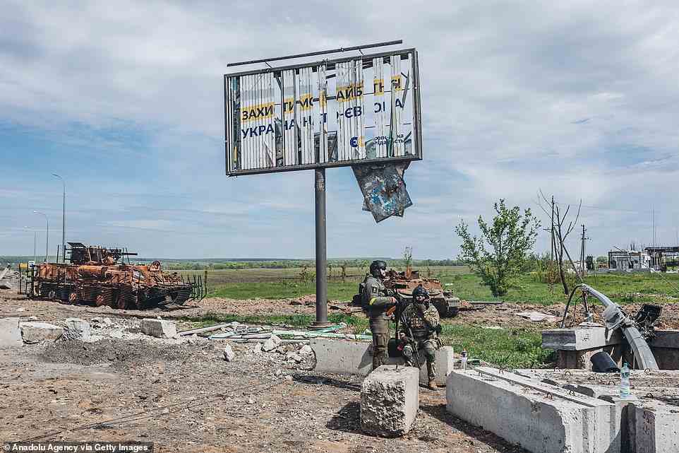 Two Ukrainian soldier keep watch at a checkpoint as a burnt-out tank is seen behind in Kharkiv, Ukraine