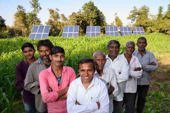 ein Foto von 8 Männern, die in AV-Form vor einem Feld mit Getreide und Sonnenkollektoren stehen