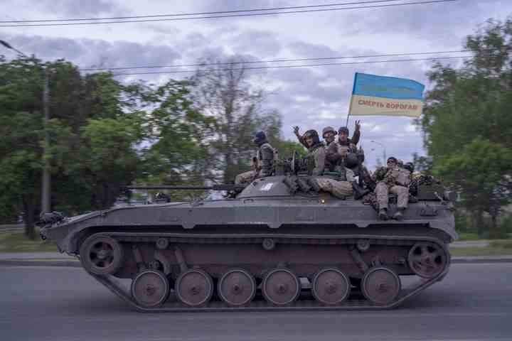 Ukrainischer Soldat schwenkt eine Fahne mit dem Schreiben von Lesungen auf Ukrainisch "Ehre der Ukraine," oben, und "Tod den Feinden" während sie am 16. Mai 2022 auf einem Panzer in der Region Charkiw in der Ostukraine fahren. 
