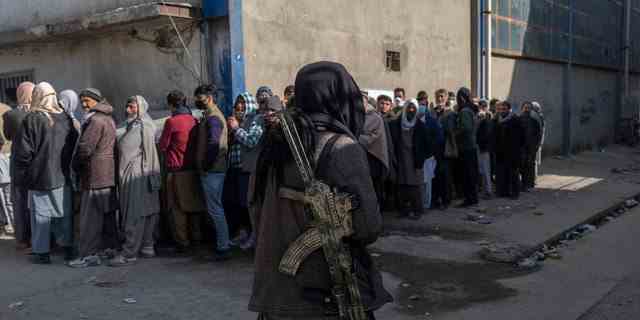 Ein Taliban-Kämpfer sichert das Gebiet, während Menschen Schlange stehen, um Bargeld bei einer vom Welternährungsprogramm organisierten Geldverteilung in Kabul, Afghanistan, am 17. November 2021 zu erhalten.