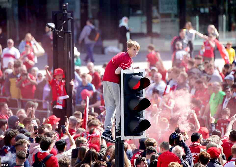 A Liverpool fan climbs a traffic light ahead to get a better view of the trophy parade through the city