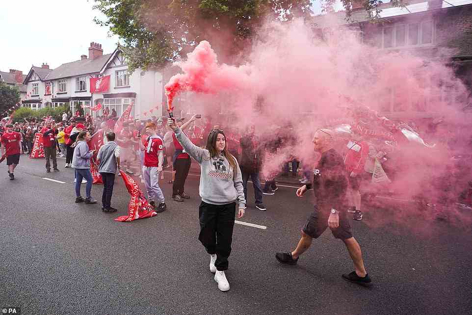 A Liverpool fan stands in front of a group wearing football shirts, while holding a red smoke flare