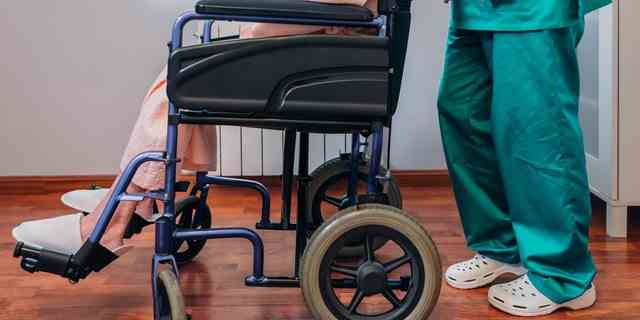 Ärztin, die ältere Patientin im Rollstuhl trägt